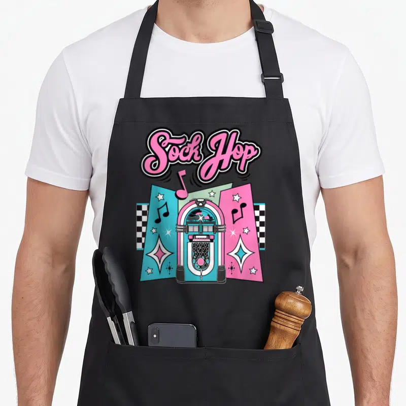 Costume 50s rockabilly apron - Pink Sock Hop script above jukebox flanked by teal and pink panels with checkerboard — shown on a black cotton canvas apron against a white background