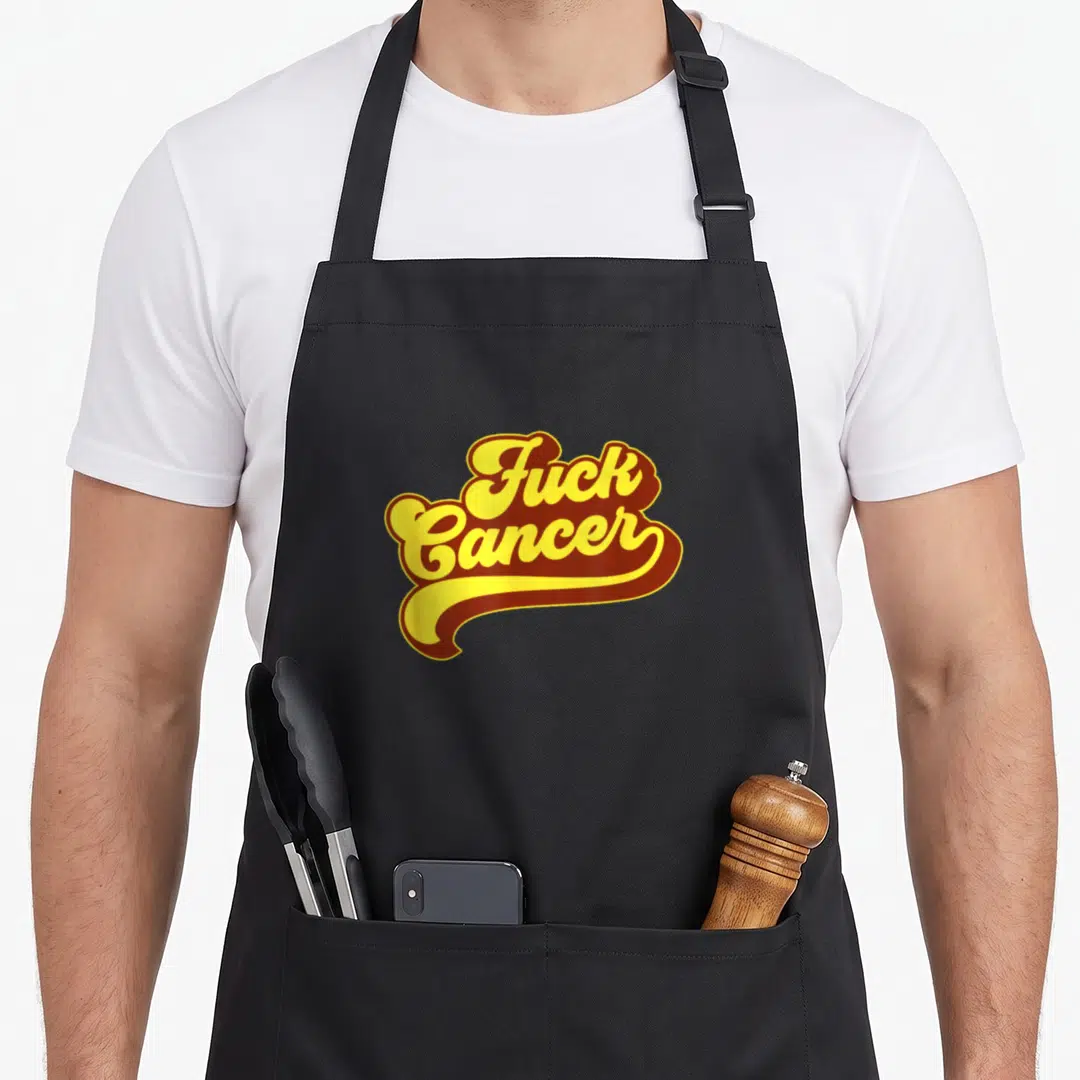 Funny cancer survivor apron - Yellow and brown retro script reading Fuck Cancer with a decorative underline swoosh — shown on a black cotton canvas apron against a white background