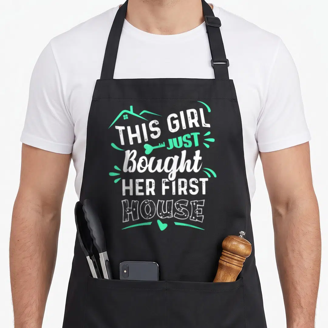 Bought owner novelty apron - White and mint green text reading THIS GIRL JUST Bought HER FIRST HOUSE with house outline — shown on a black cotton canvas apron against a white background