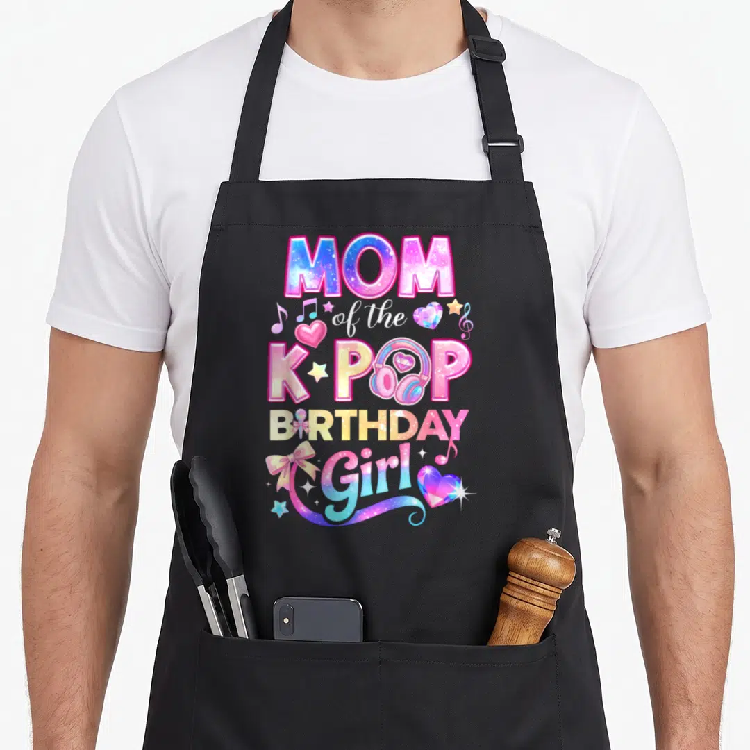 Cute pop korean apron - MOM of the K-POP BIRTHDAY Girl text with headphones and galaxy print hearts stars — shown on a black cotton canvas apron against a white background