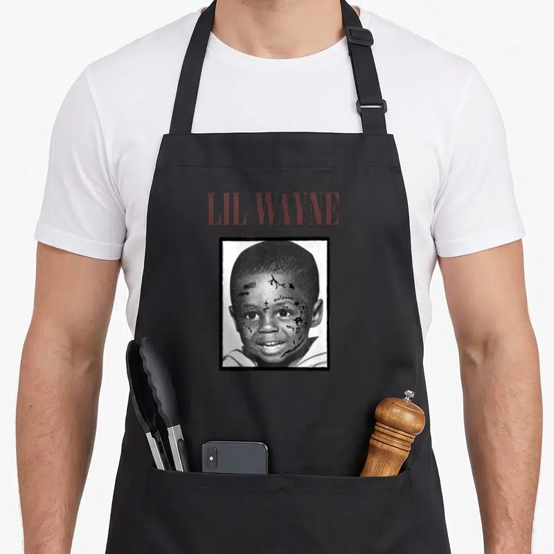 Lil concert apron - LIL WAYNE text above tattooed smiling child face in black bordered square — shown on a black cotton canvas apron against a white background