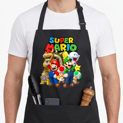 Funny shot apron - SUPER MARIO text above Mario, Luigi, Bowser, Toad, Boo, coin, star in red blue green yellow white — shown on a black cotton canvas apron against a white background