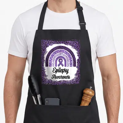 Epilepsy leopard apron - Purple leopard frame with heart rainbow, ribbon, and Epilepsy Awareness text — shown on a black cotton canvas apron against a white background