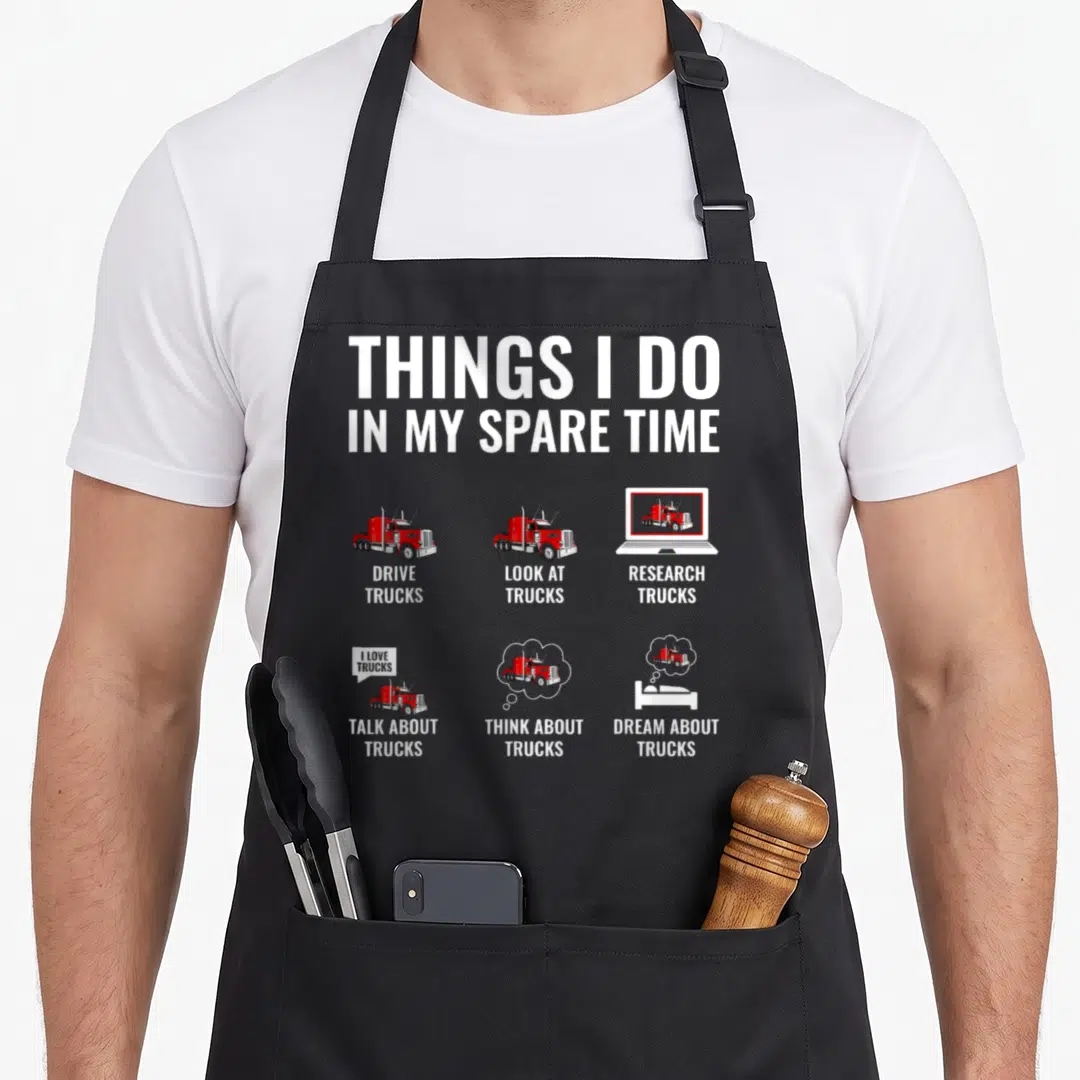 Spare semi truck apron - THINGS I DO IN MY SPARE TIME text with six red truck illustrations on grey background — shown on a black cotton canvas apron against a white background