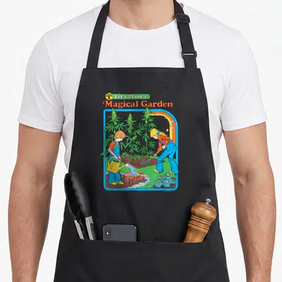 Steven mushroom apron - Two children gardening among cannabis plants and mushrooms under Let's Plant a Magical Garden — shown on a black cotton canvas apron against a white background