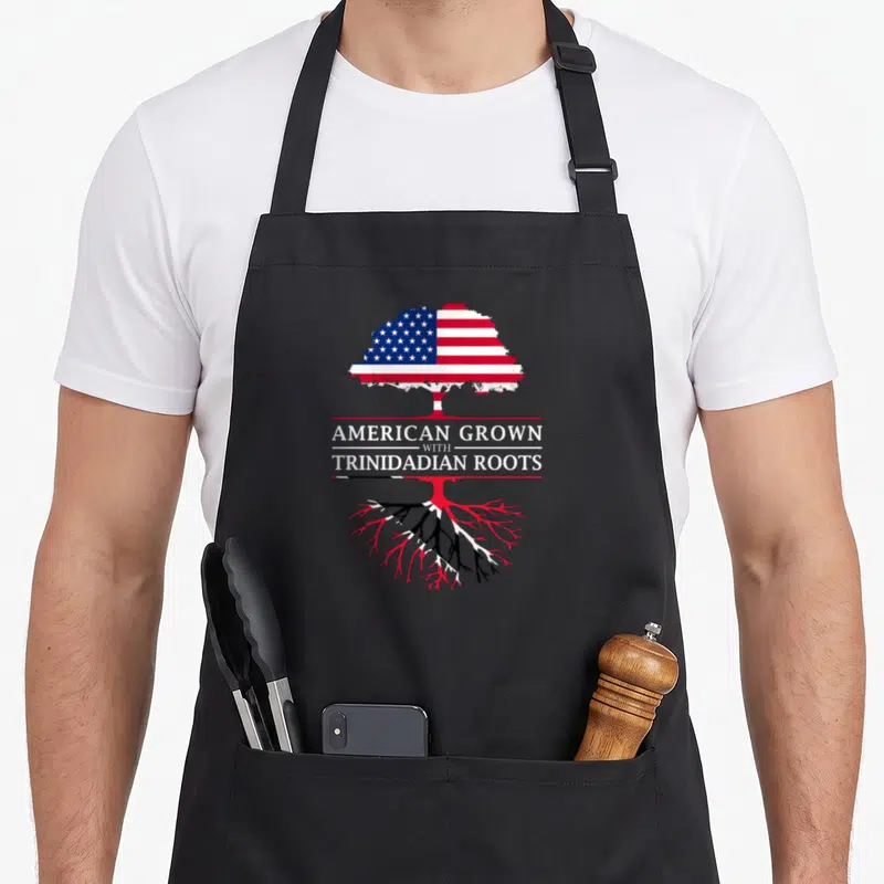 Grown trinidadian pride apron - Tree with US flag leaves and Trinidad flag roots overlaid with American Grown — shown on a black cotton canvas apron against a white background