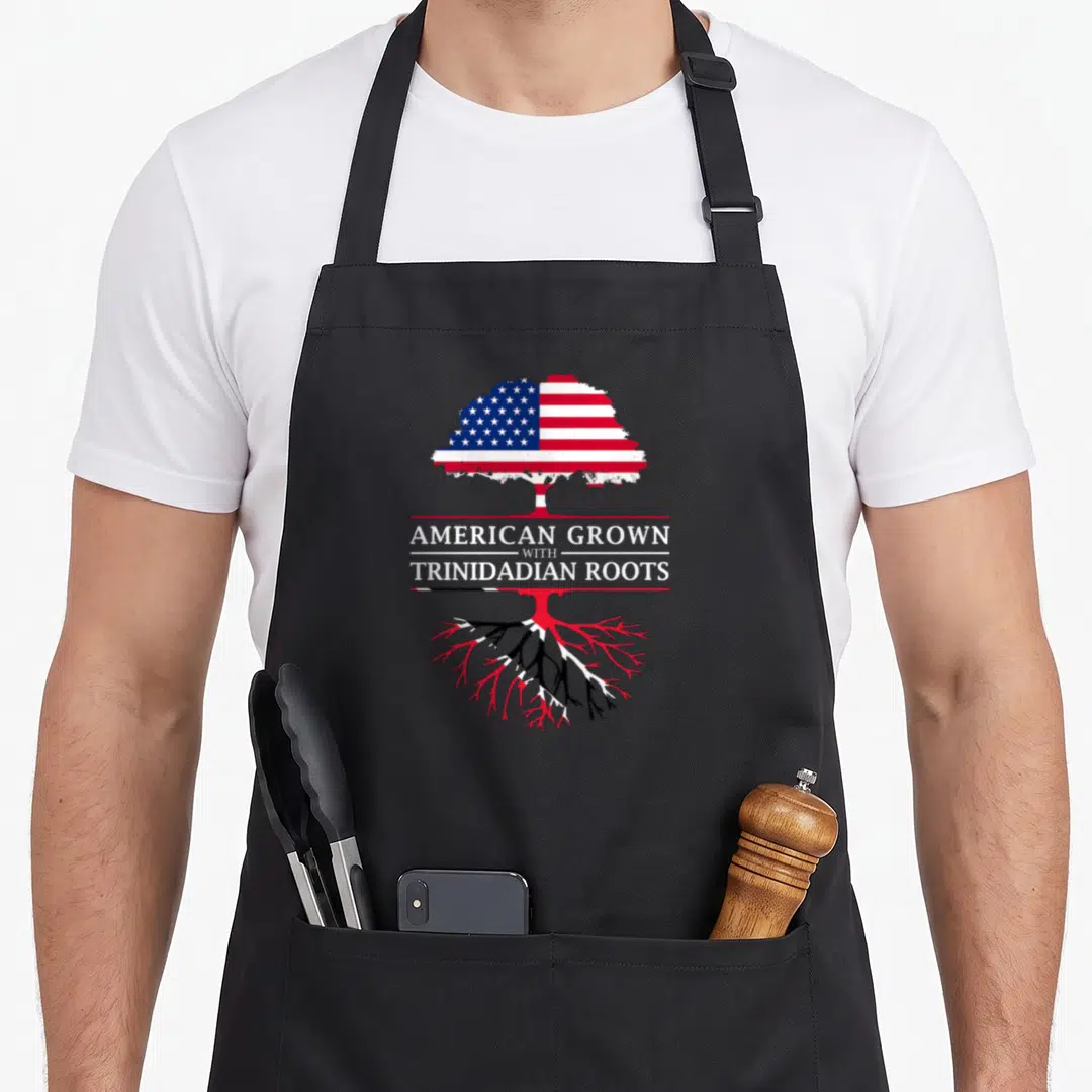 Grown trinidadian pride apron - Tree with US flag leaves and Trinidad flag roots overlaid with American Grown — shown on a black cotton canvas apron against a white background