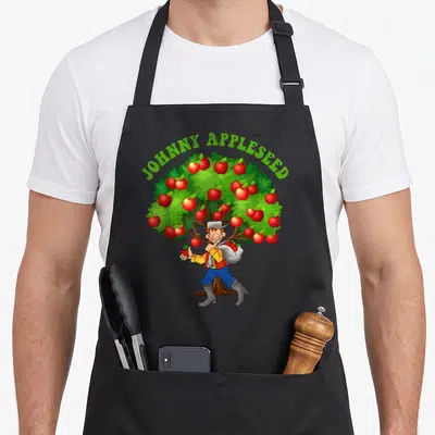 Johnny apple apron - Cartoon man holding red apples under green JOHNNY APPLESEED text near a tree — shown on a black cotton canvas apron against a white background