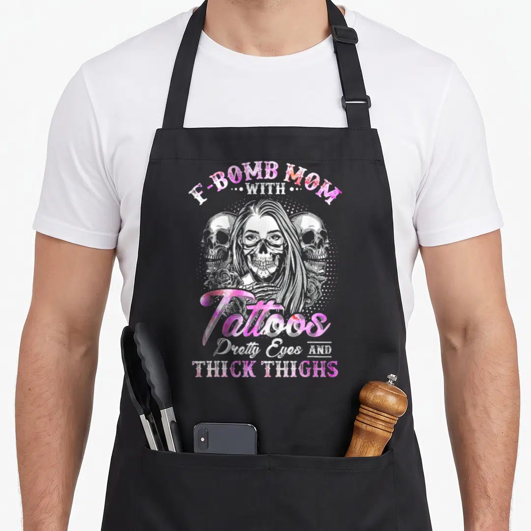 Thick tattoo apron - Skeleton woman with E-Bomb Mom text, pink lettering, two skulls and roses — shown on a black cotton canvas apron against a white background