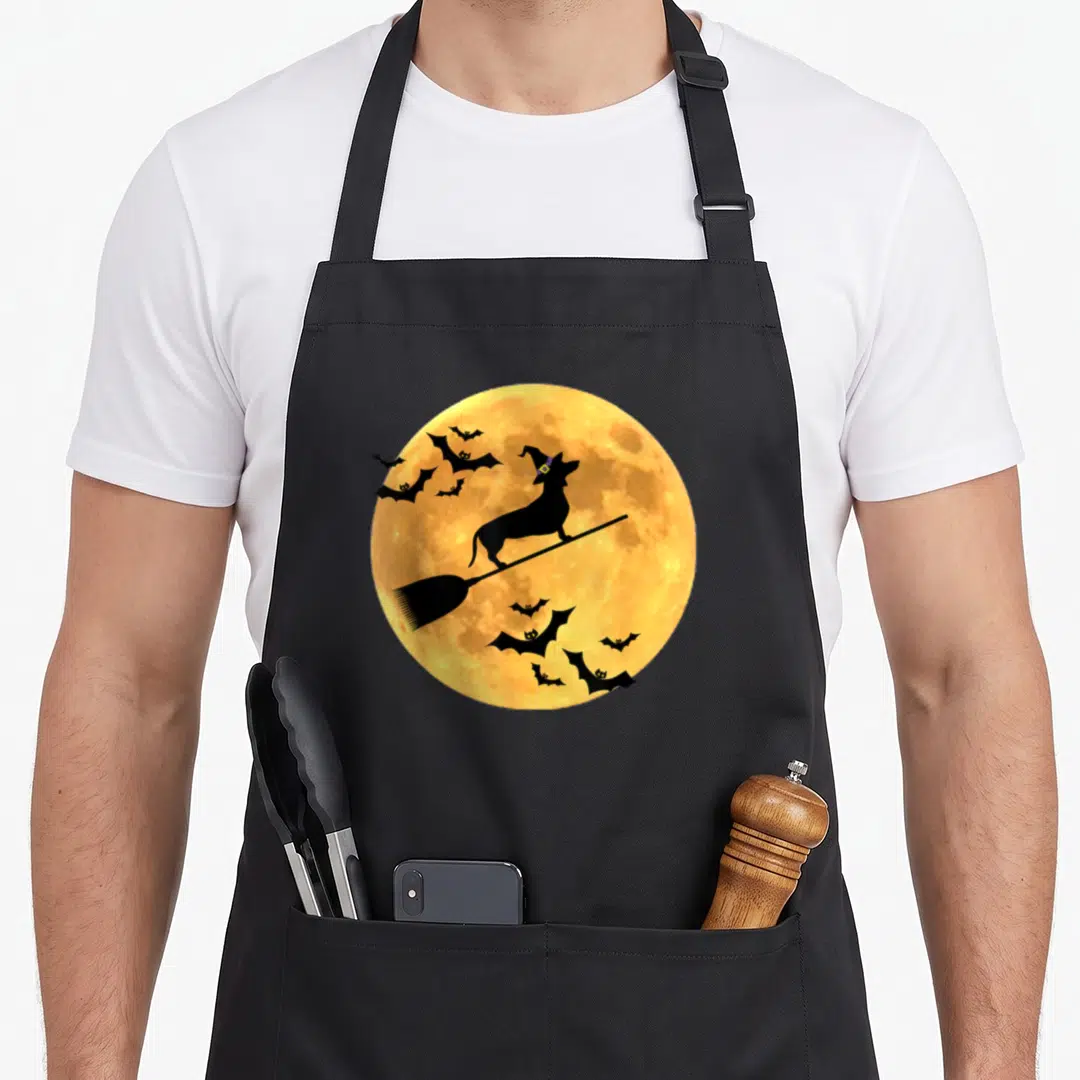 Witch cheap halloween aprons - Black dachshund silhouette on broomstick in front of yellow full moon with flying bats — shown on a black cotton canvas apron against a white background