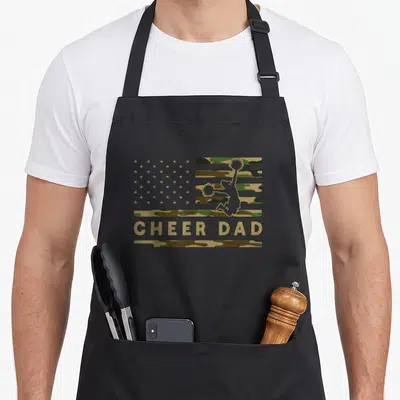 Cheer camo apron - CHEER DAD text under cheerleader silhouette on camo flag — shown on a black cotton canvas apron against a white background