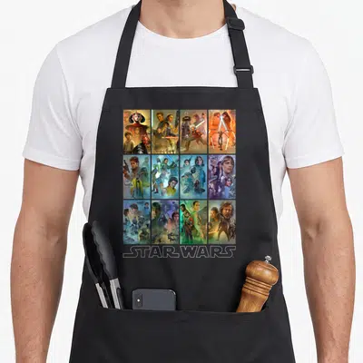 Celebration wars new apron - Grid of 12 Star Wars character posters with white STAR WARS text at bottom — shown on a black cotton canvas apron against a white background