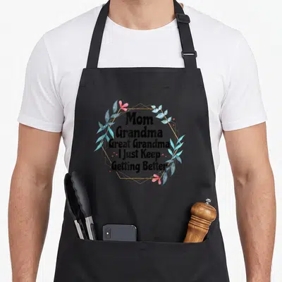 Getting great grandma apron - Mom Grandma Great Grandma I Just Keep Getting Better text with blue watercolor leaves — shown on a black cotton canvas apron against a white background