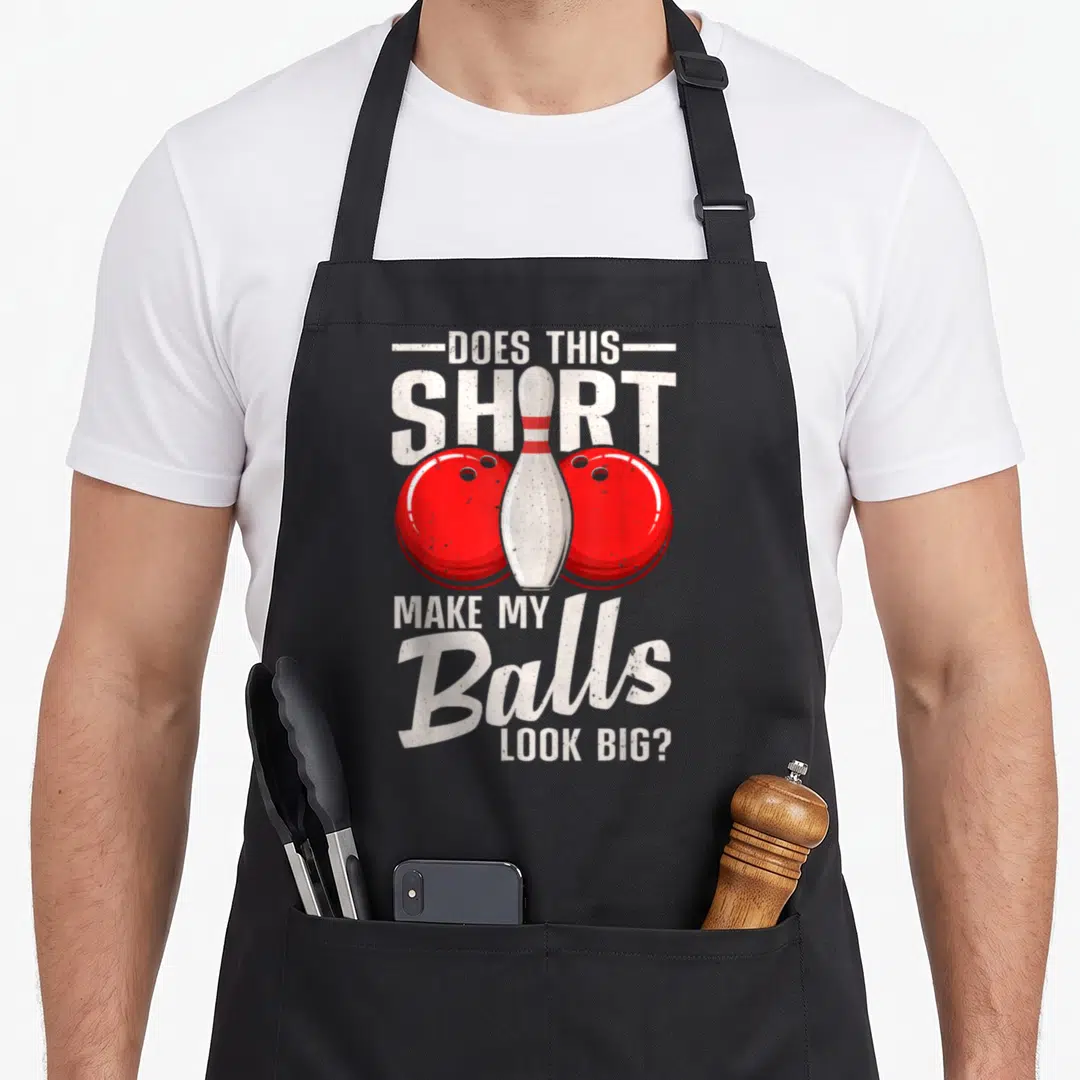Ball bowling green apron - Distressed text DOES THIS SHIRT MAKE MY BALLS LOOK BIG with red balls and white pin — shown on a black cotton canvas apron against a white background