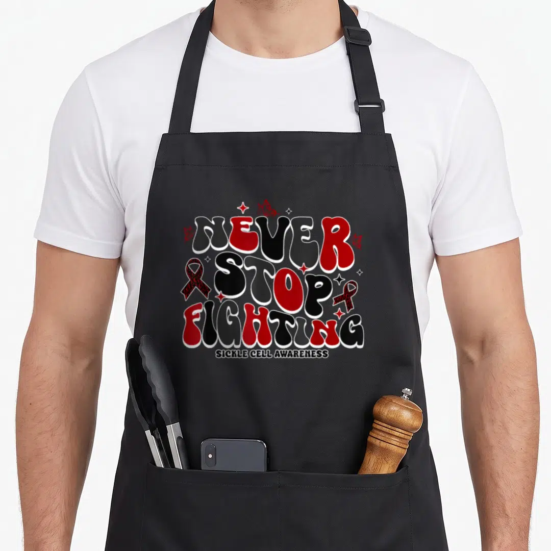 Stop sickle cell awareness apron - NEVER STOP FIGHTING text with red ribbons and butterflies in bubble font — shown on a black cotton canvas apron against a white background