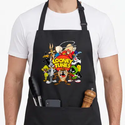 Toon character aprons - Looney Tunes characters clustered around a red circle with yellow LOONEY TUNES text in cartoon — shown on a black cotton canvas apron against a white background