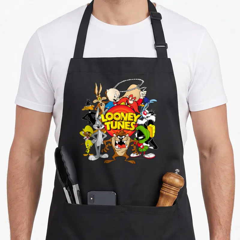 Toon character aprons - Looney Tunes characters clustered around a red circle with yellow LOONEY TUNES text in cartoon — shown on a black cotton canvas apron against a white background