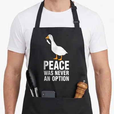 Peace meme apron - Cartoon goose holding a knife in beak above three lines of text peace was never an option — shown on a black cotton canvas apron against a white background