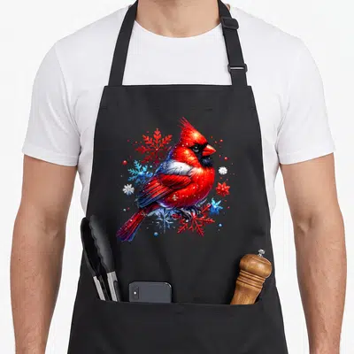 Snowflake the floral apron - Realistic red cardinal perched among red, blue, and white snowflakes with small berries — shown on a black cotton canvas apron against a white background