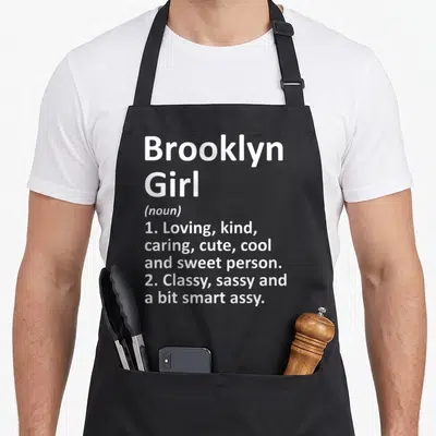Vintage brooklyn new york apron - White text reading Brooklyn Girl noun definition listing sweet and sassy traits — shown on a black cotton canvas apron against a white background