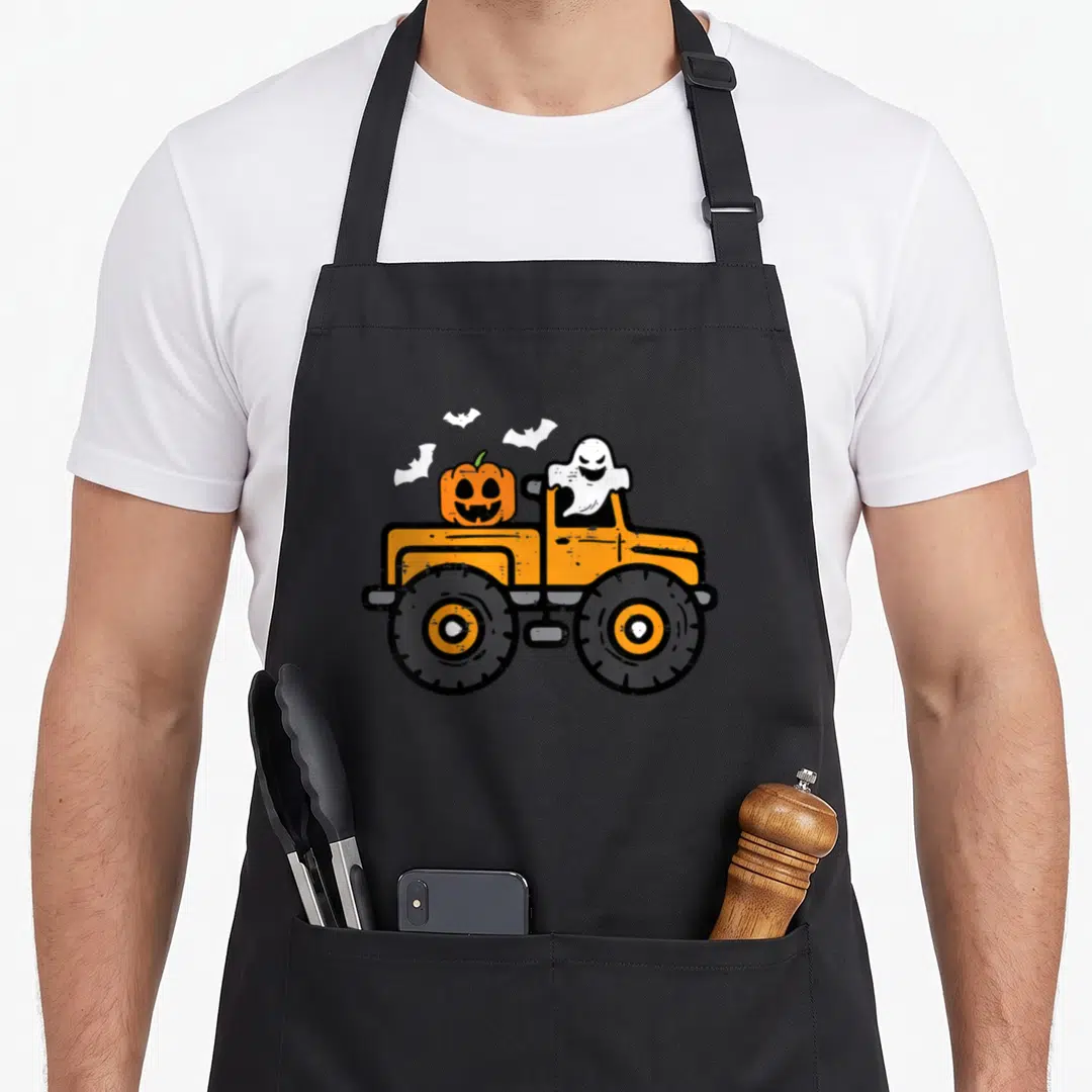 Monster pumpkin apron - Orange monster truck with white ghost driver and pumpkin cargo flanked by three bats — shown on a black cotton canvas apron against a white background