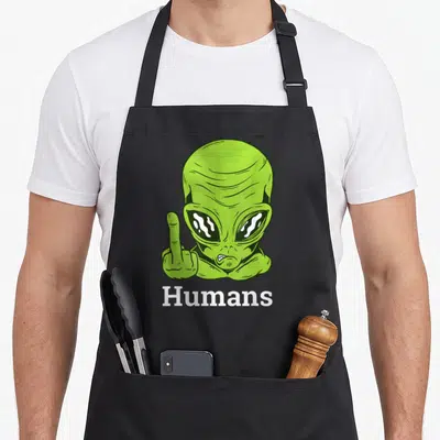 Ufo funny alien apron - Green cartoon alien raising middle finger with white Humans text below — shown on a black cotton canvas apron against a white background