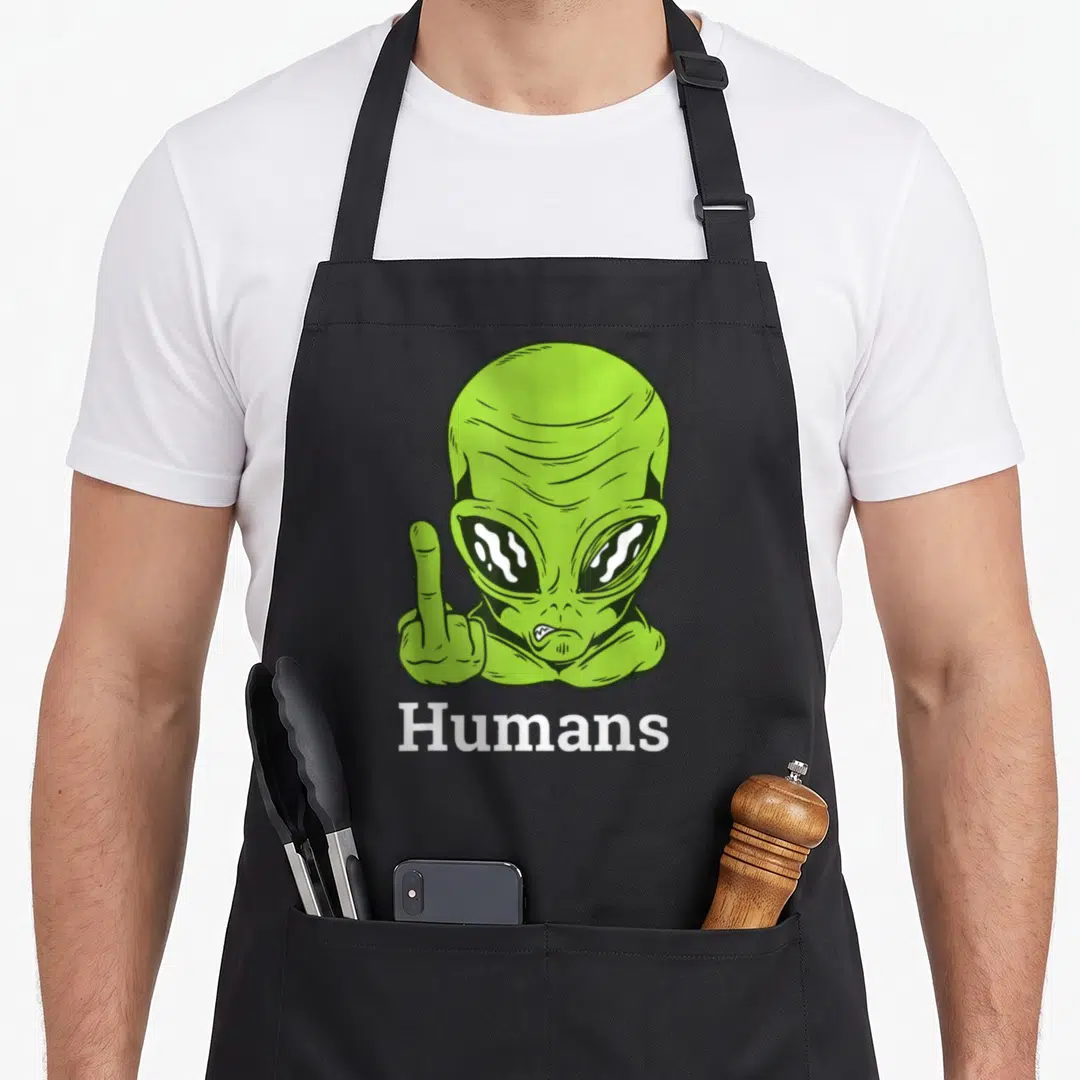 Ufo funny alien apron - Green cartoon alien raising middle finger with white Humans text below — shown on a black cotton canvas apron against a white background