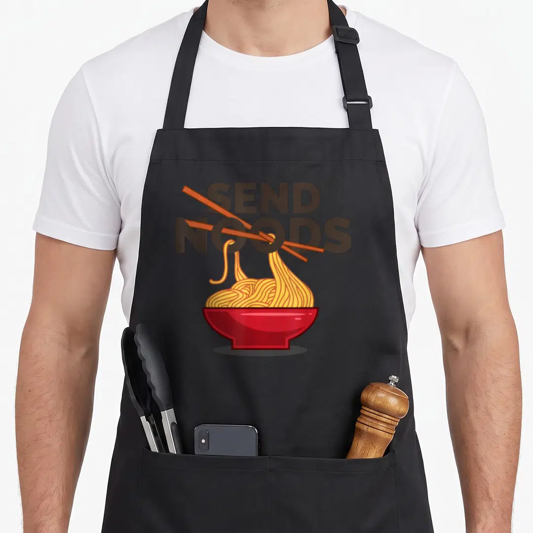 Send noodling apron - Cartoon red bowl with yellow noodles and brown chopsticks under SEND NOODS text — shown on a black cotton canvas apron against a white background