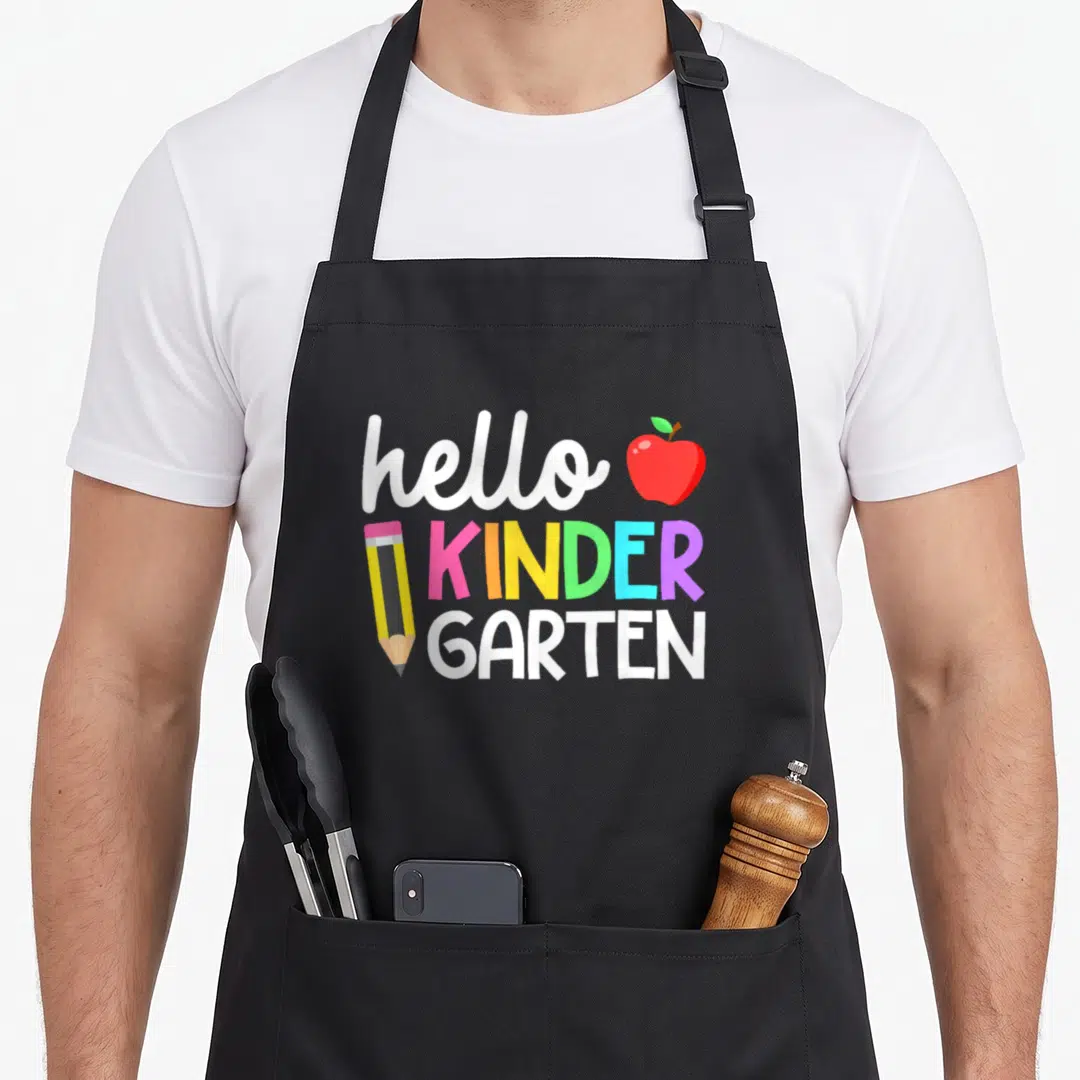 Hello cute teacher aprons - Hello Kinder Garten text with red apple and yellow pencil in cartoon style — shown on a black cotton canvas apron against a white background