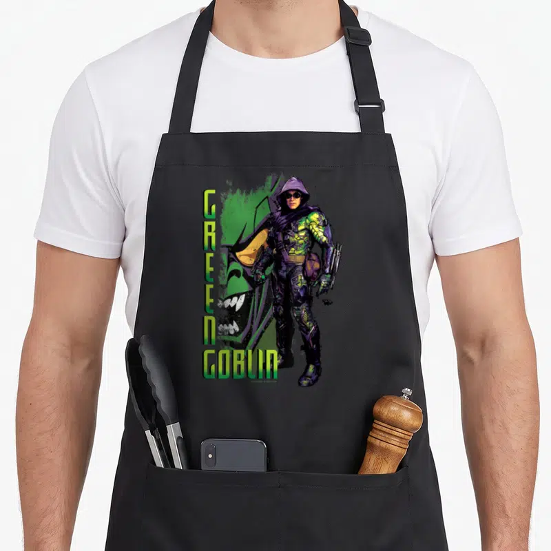 Supervillain goblin apron - Vertical GREEN GOBLIN text beside hooded character with large green face background — shown on a black cotton canvas apron against a white background