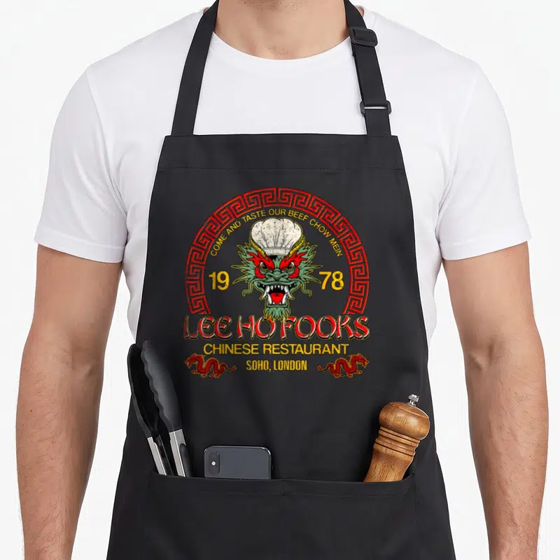 Fook chinese apron - Retro Lee Ho Fooks dragon chef hat 1978 Soho London text red yellow green — shown on a black cotton canvas apron against a white background