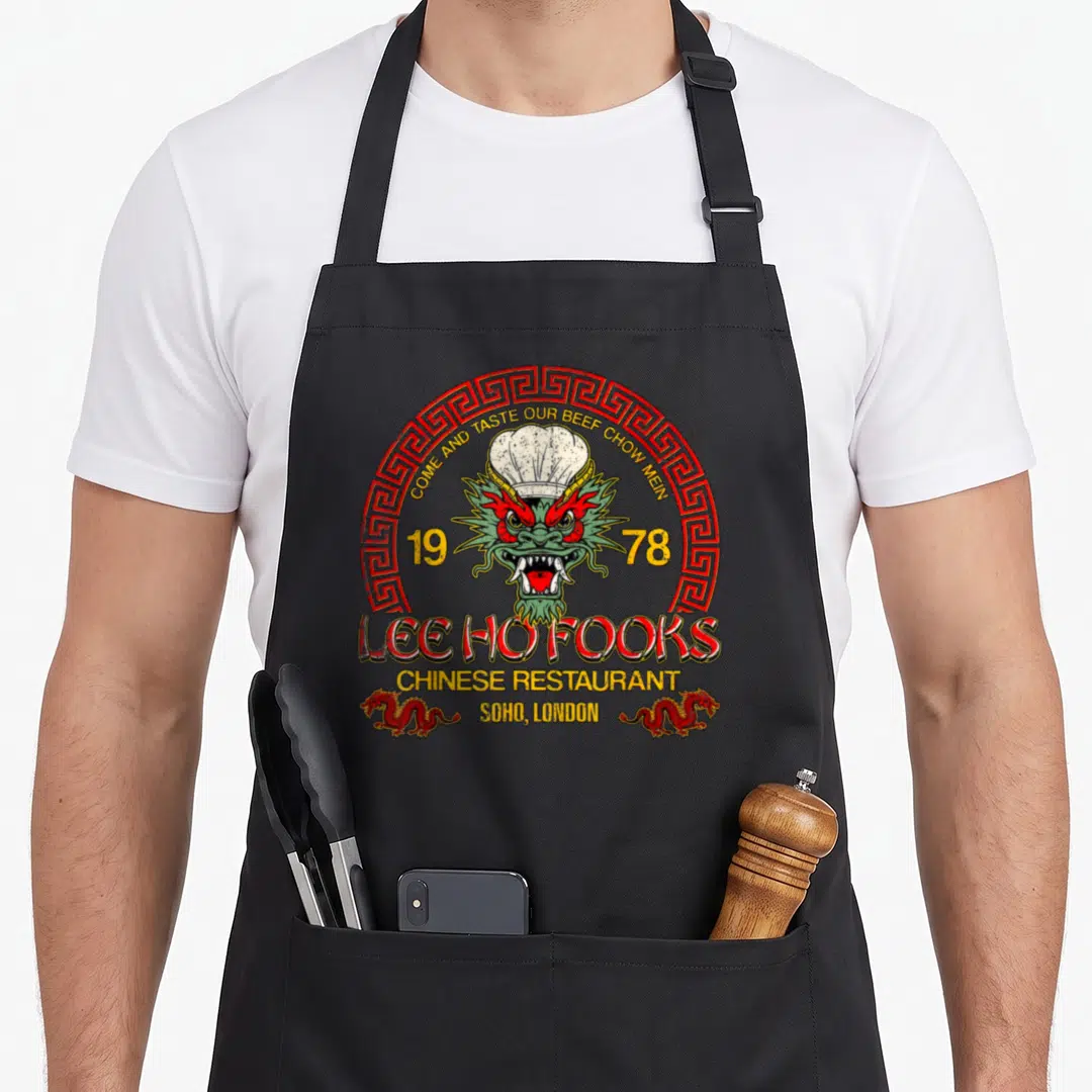 Fook chinese apron - Retro Lee Ho Fooks dragon chef hat 1978 Soho London text red yellow green — shown on a black cotton canvas apron against a white background