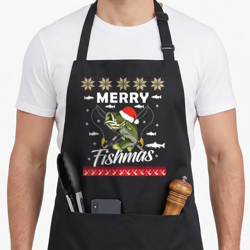 Fishing xmas apron - Merry Fishmas text with Santa hat fish and crossed rods — shown on a black cotton canvas apron against a white background