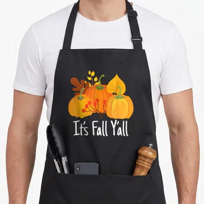 Yall thanksgiving apron - Cartoon orange pumpkins red berries and white It's Fall Y'all text — shown on a black cotton canvas apron against a white background