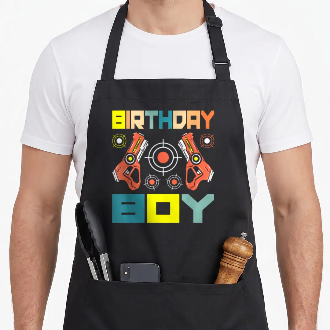 Tag birthday apron - BIRTHDAY BOY text with two toy guns and four targets in red yellow blue green and white — shown on a black cotton canvas apron against a white background