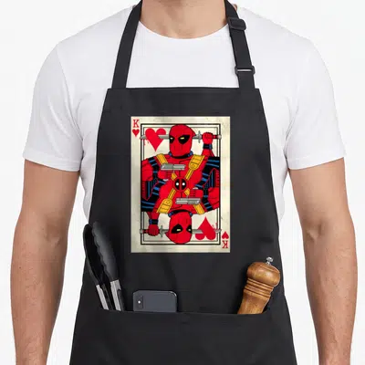 Merc king apron - Mirrored Deadpool playing card art in red black white yellow with K and hearts — shown on a black cotton canvas apron against a white background