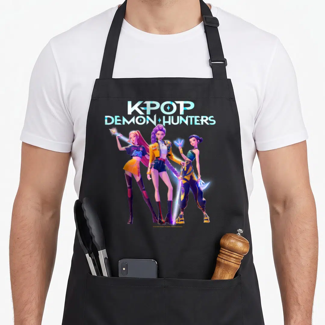 Huntrix hunter apron - KPOP DEMON HUNTERS text above three women in blue yellow purple cartoon outfits — shown on a black cotton canvas apron against a white background