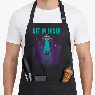 Loser fiction lover apron - Teal text GET IN LOSER above grey UFO lifting person from purple forest with beam — shown on a black cotton canvas apron against a white background