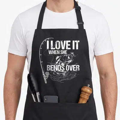 Bend novelty apron - White distressed text I love it when she bends over with a jumping fish and fishing rod — shown on a black cotton canvas apron against a white background
