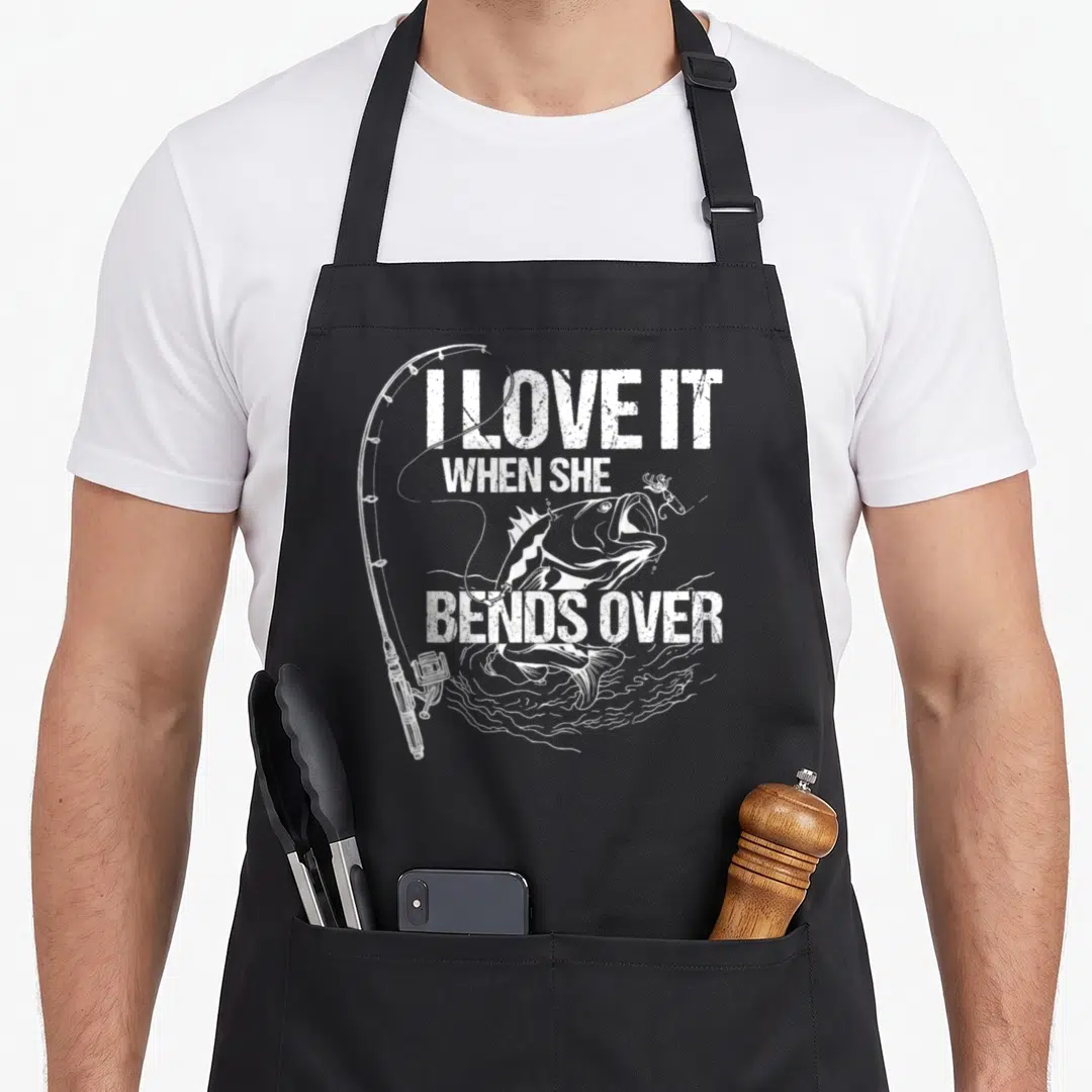 Bend novelty apron - White distressed text I love it when she bends over with a jumping fish and fishing rod — shown on a black cotton canvas apron against a white background