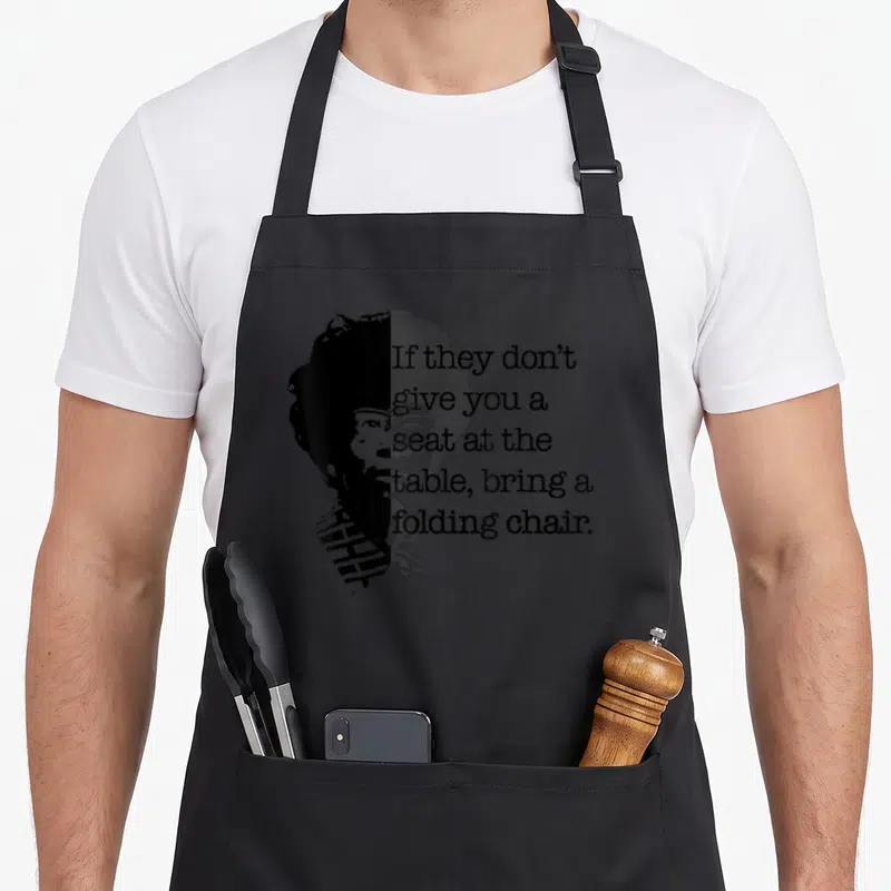 Bring table apron - Stacked text next to black and grey two-tone woman portrait — shown on a black cotton canvas apron against a white background