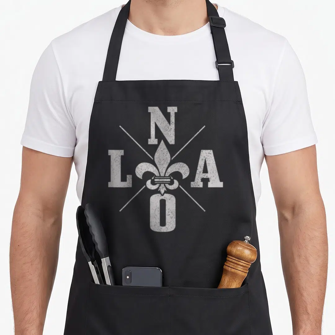 Nola pride apron - White distressed fleur-de-lis surrounded by N L A O letters and diagonal lines — shown on a black cotton canvas apron against a white background