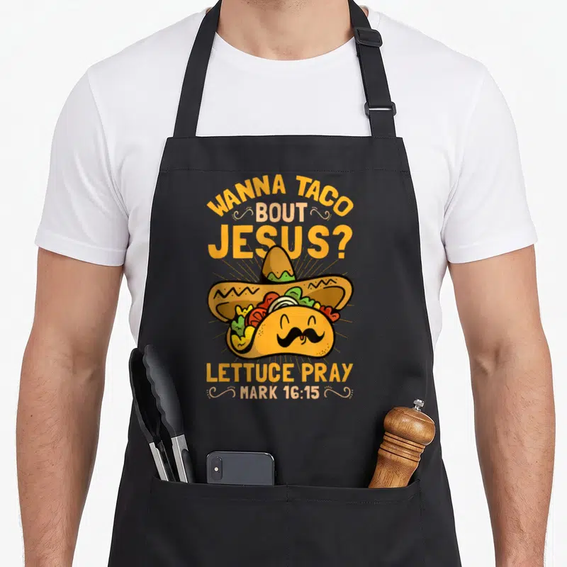 Taco bout christian apron - Cartoon taco with sombrero and mustache surrounded by yellow and orange punny text — shown on a black cotton canvas apron against a white background