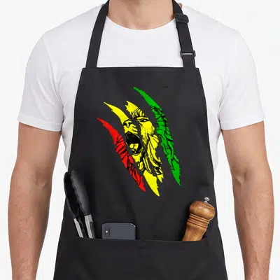 Root lions apron - Cartoon lion face seen through red, yellow, and green diagonal claw marks — shown on a black cotton canvas apron against a white background