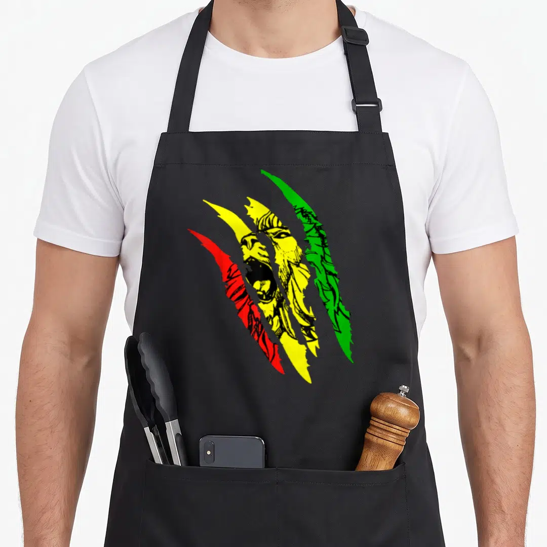Root lions apron - Cartoon lion face seen through red, yellow, and green diagonal claw marks — shown on a black cotton canvas apron against a white background
