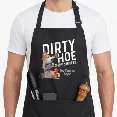 Supply the dirty apron - Retro pin-up woman pouring teal watering can beside white DIRTY HOE text with red tulips — shown on a black cotton canvas apron against a white background