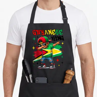 Guyanese king apron - Cartoon boy dabbing in Guyana flag colors with GUYANESE KING GUYANA text — shown on a black cotton canvas apron against a white background