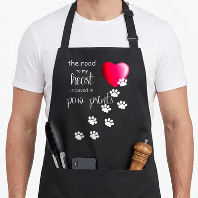 Road paw print apron - White text and red heart with white paw prints trailing down — shown on a black cotton canvas apron against a white background