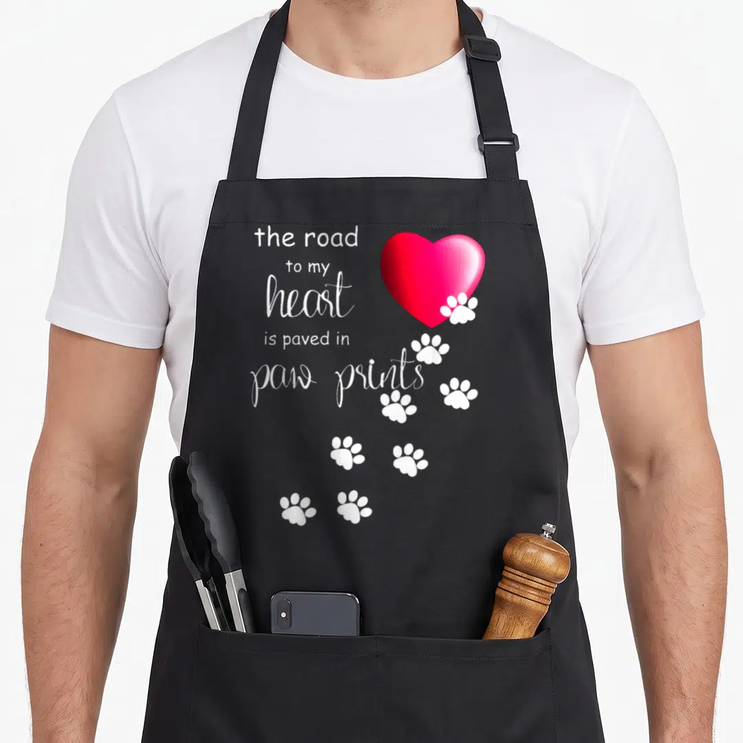 Road paw print apron - White text and red heart with white paw prints trailing down — shown on a black cotton canvas apron against a white background