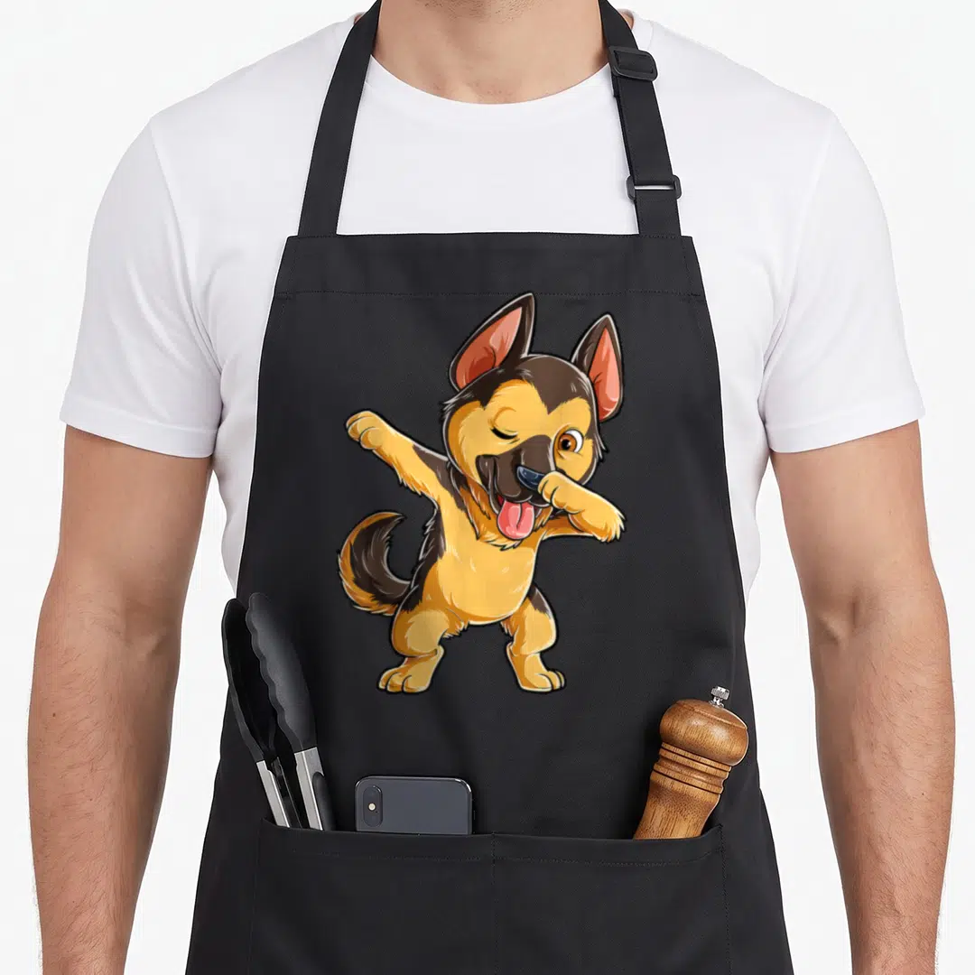 Dabbing dog mom apron - Cartoon tan and black German Shepherd standing on two legs dabbing with pink tongue out — shown on a black cotton canvas apron against a white background